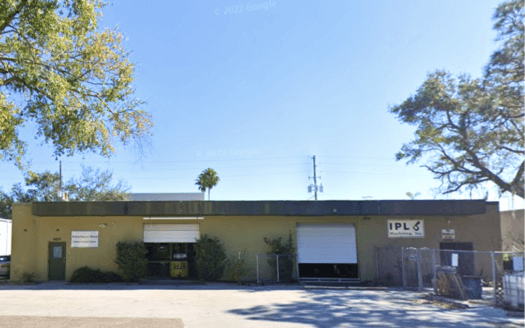 Single-story commercial property with two large garage doors, trees on both sides, and a "SOLD" label in the top right corner. Signs are visible on the front wall of this industrial commercial real estate.