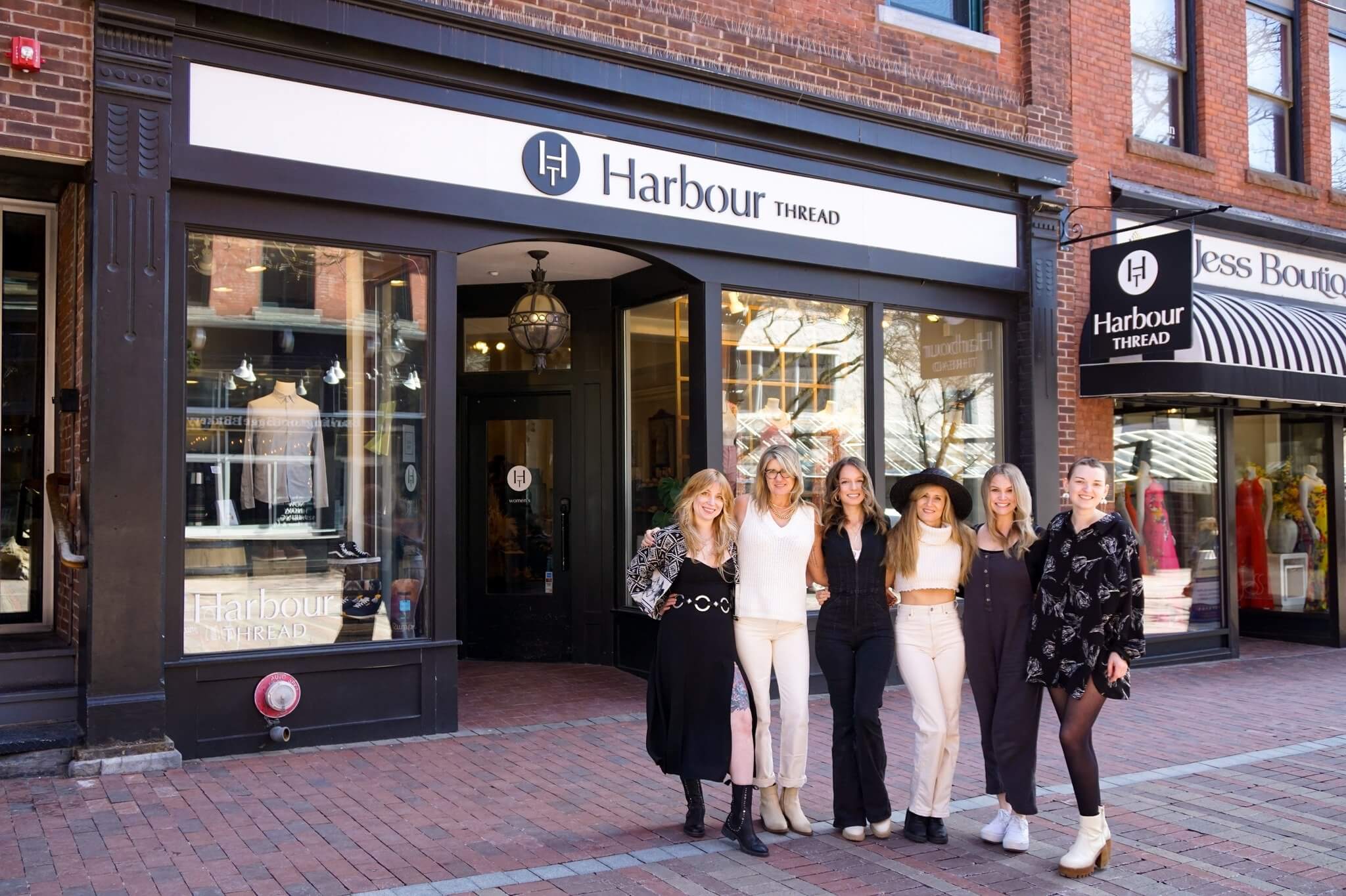 Five women stand in front of the Harbour Thread clothing store, a vibrant commercial property on a brick-paved street, posing for a group photo.