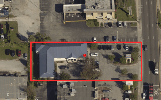 Aerial view of a commercial property and parking lot outlined in red, surrounded by other businesses, cars, and a main road—ideal for those seeking prime commercial real estate.