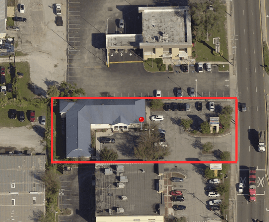 Aerial view of a commercial property and parking lot outlined in red, surrounded by other businesses, cars, and a main road—ideal for those seeking prime commercial real estate.