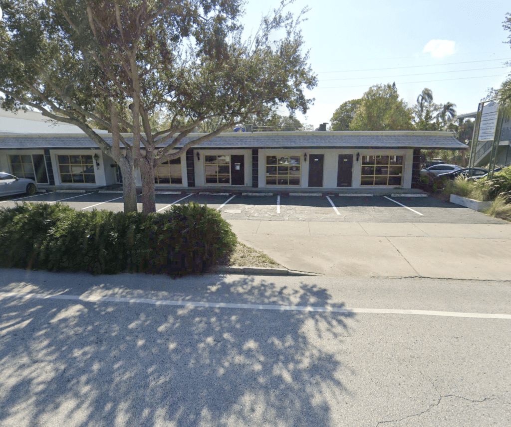 Single-story commercial property featuring a row of windows and doors, empty parking spaces in front, and trees and bushes lining the sidewalk—ideal for those seeking quality commercial real estate.