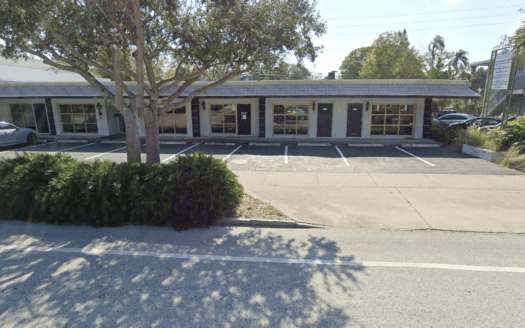 Single-story commercial property featuring a row of windows and doors, empty parking spaces in front, and trees and bushes lining the sidewalk—ideal for those seeking quality commercial real estate.