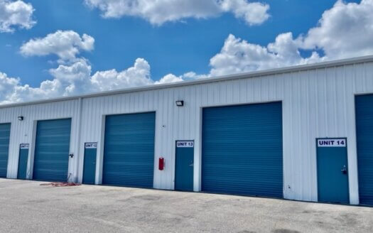 Row of white self-storage units with blue roll-up doors and unit numbers 12, 13, and 14 visible under a partly cloudy sky—ideal commercial property for your storage or commercial real estate needs.