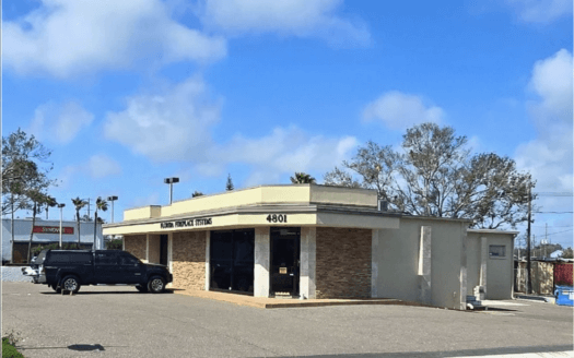 Single-story commercial property with a brick facade and flat roof, labeled "4801." A black SUV is parked in front, with trees and a blue sky in the background.