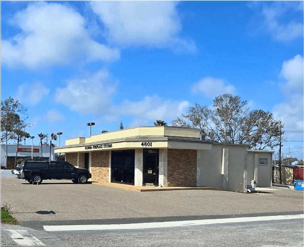 Single-story commercial property with a brick facade and flat roof, labeled "4801." A black SUV is parked in front, with trees and a blue sky in the background.