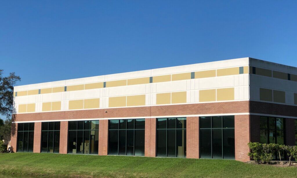 A two-story commercial property with large windows on the ground floor, a brick base, and a beige upper facade, set against a clear blue sky.