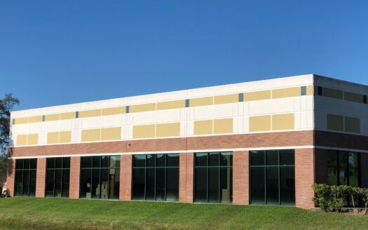 A two-story commercial property with large windows on the ground floor, a brick base, and a beige upper facade, set against a clear blue sky.