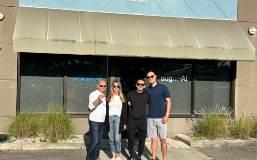 Four people pose under a tan awning in front of a building with address 11286 on US HWY 19 Clearwater; two glass doors read "MONTKUSH" and "sugar AI," highlighting these leased property Clearwater commercial units.