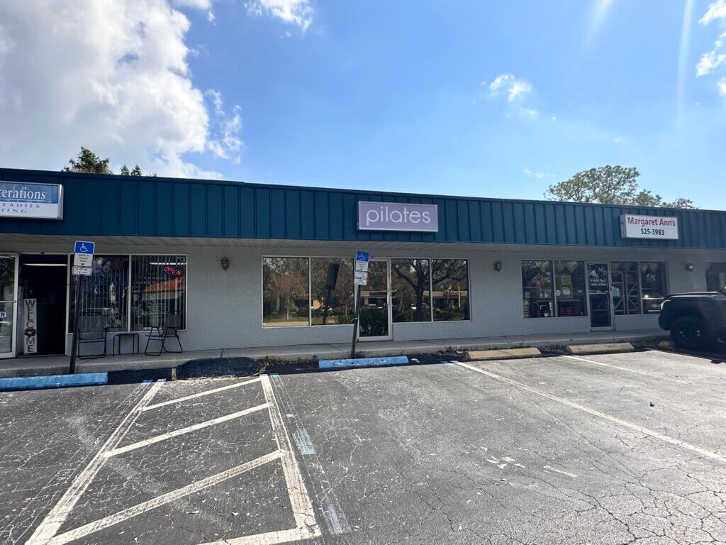 A small commercial property with a parking lot in front, featuring a storefront with a sign that reads "pilates" and adjacent businesses in this bustling strip mall.