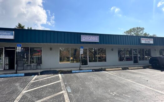 A small commercial property with a parking lot in front, featuring a storefront with a sign that reads "pilates" and adjacent businesses in this bustling strip mall.