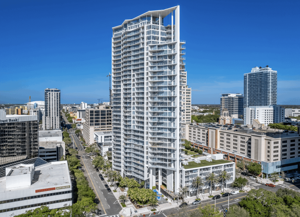 A tall, modern residential high-rise with white exterior and balconies stands near 147 2nd Avenue S, Suite 210, in a cityscape of mid-rise buildings under a clear blue sky.