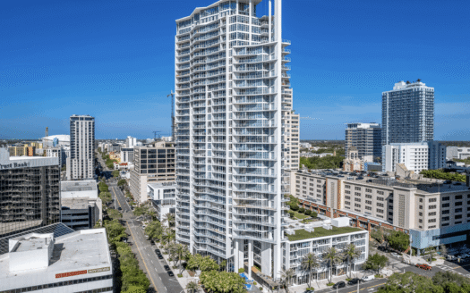A tall, modern residential high-rise with white exterior and balconies stands near 147 2nd Avenue S, Suite 210, in a cityscape of mid-rise buildings under a clear blue sky.