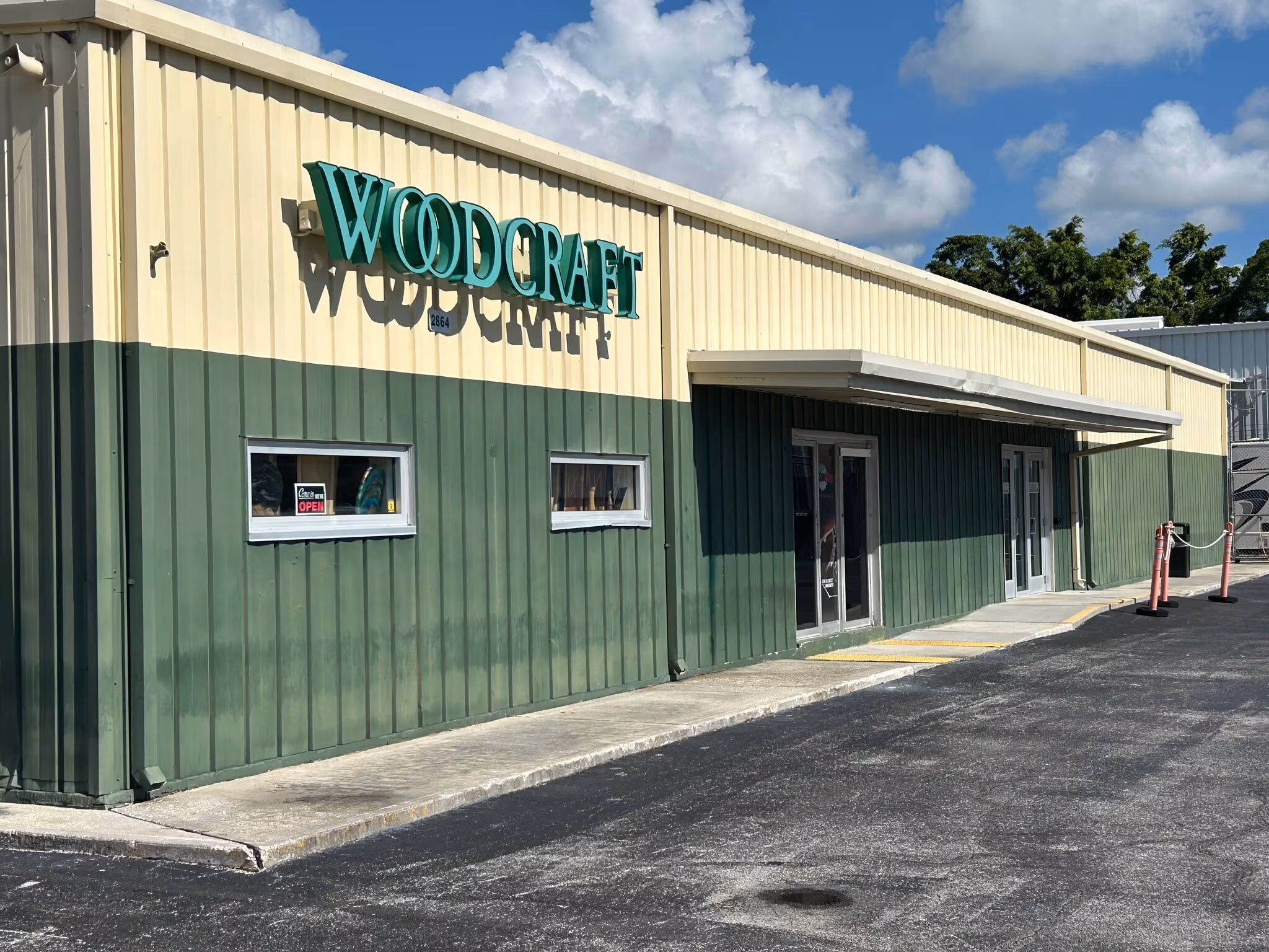A tan and green metal building, Building 3, with a sign reading "WOOD CRAFT" above the entrance, sits under a blue sky with clouds on Roosevelt Blvd.