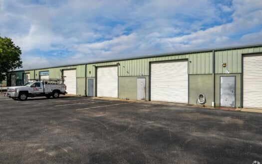 Recently sold in Clearwater FL, this long, single-story industrial building at 12820 Daniel Dr features multiple roll-up garage doors, standard doors, and sits next to a parking lot with a work truck parked on the left.
