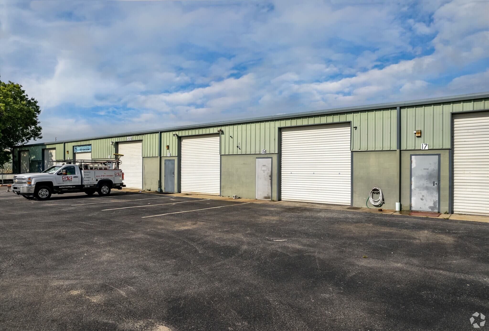 Recently sold in Clearwater FL, this long, single-story industrial building at 12820 Daniel Dr features multiple roll-up garage doors, standard doors, and sits next to a parking lot with a work truck parked on the left.