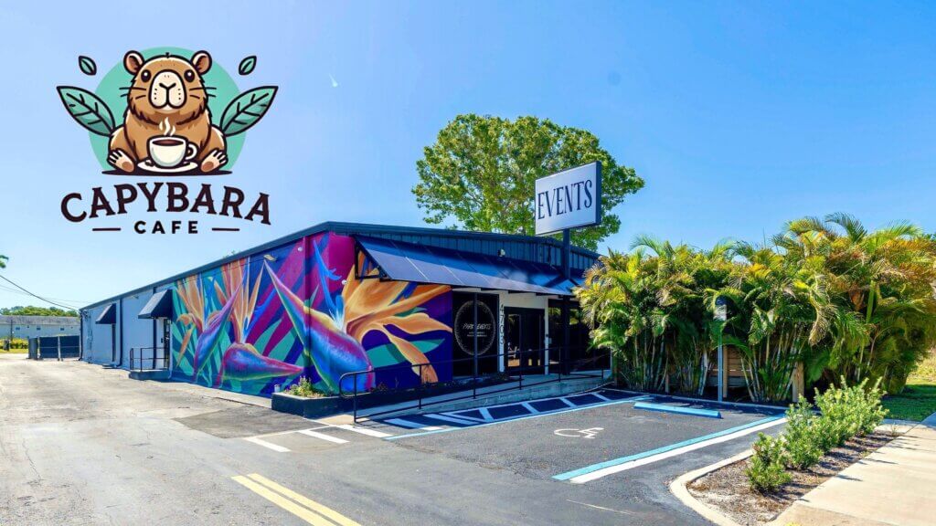 A single-story building at 4703 Park St, St. Petersburg, with a colorful mural and palm trees, featuring signage for "Capybara Cafe" and "Events" under a clear blue sky—recently sold in sunny FL.
